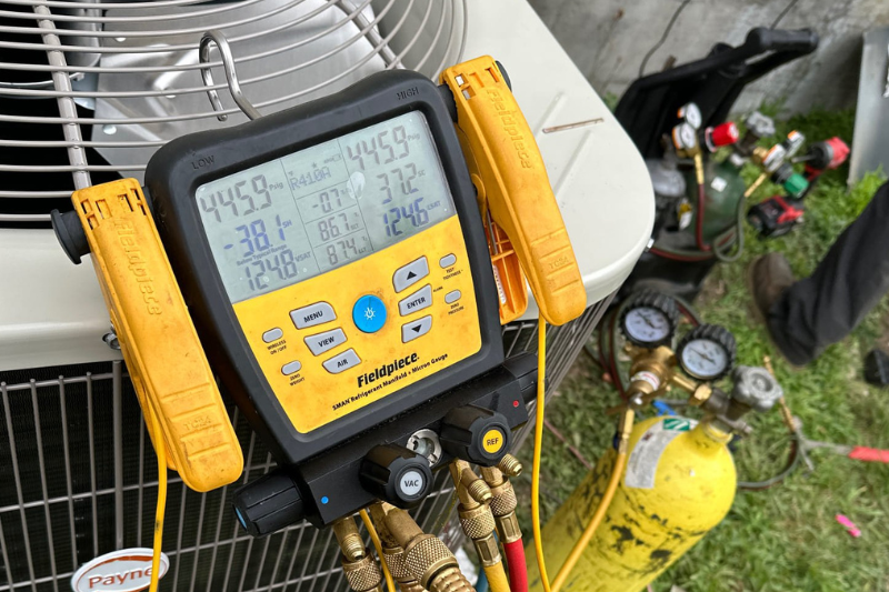 A Fieldpiece manifold gauge rests upon an outdoor HVAC condenser unit.