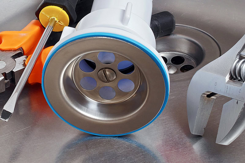4 Reasons to Clean Your Drains Before the Holidays. plumber tools and drain assembly in stainless kitchen sink.