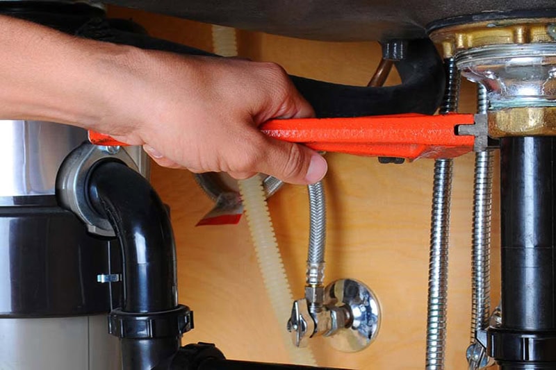 2025 Guide to Garbage Disposals. Photo of a person inspecting a garbage disposal under a sink.